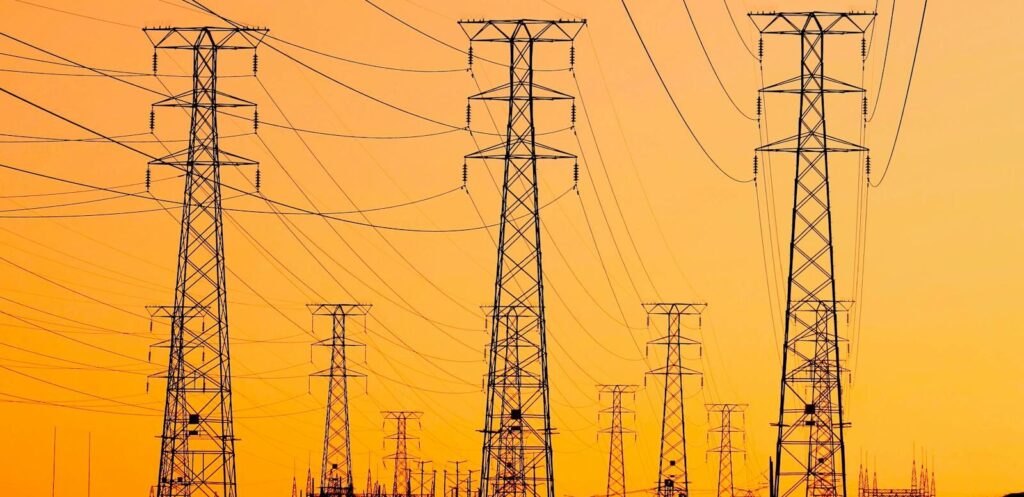 Silhouetted power lines against a vibrant orange sunset, symbolizing energy and infrastructure.